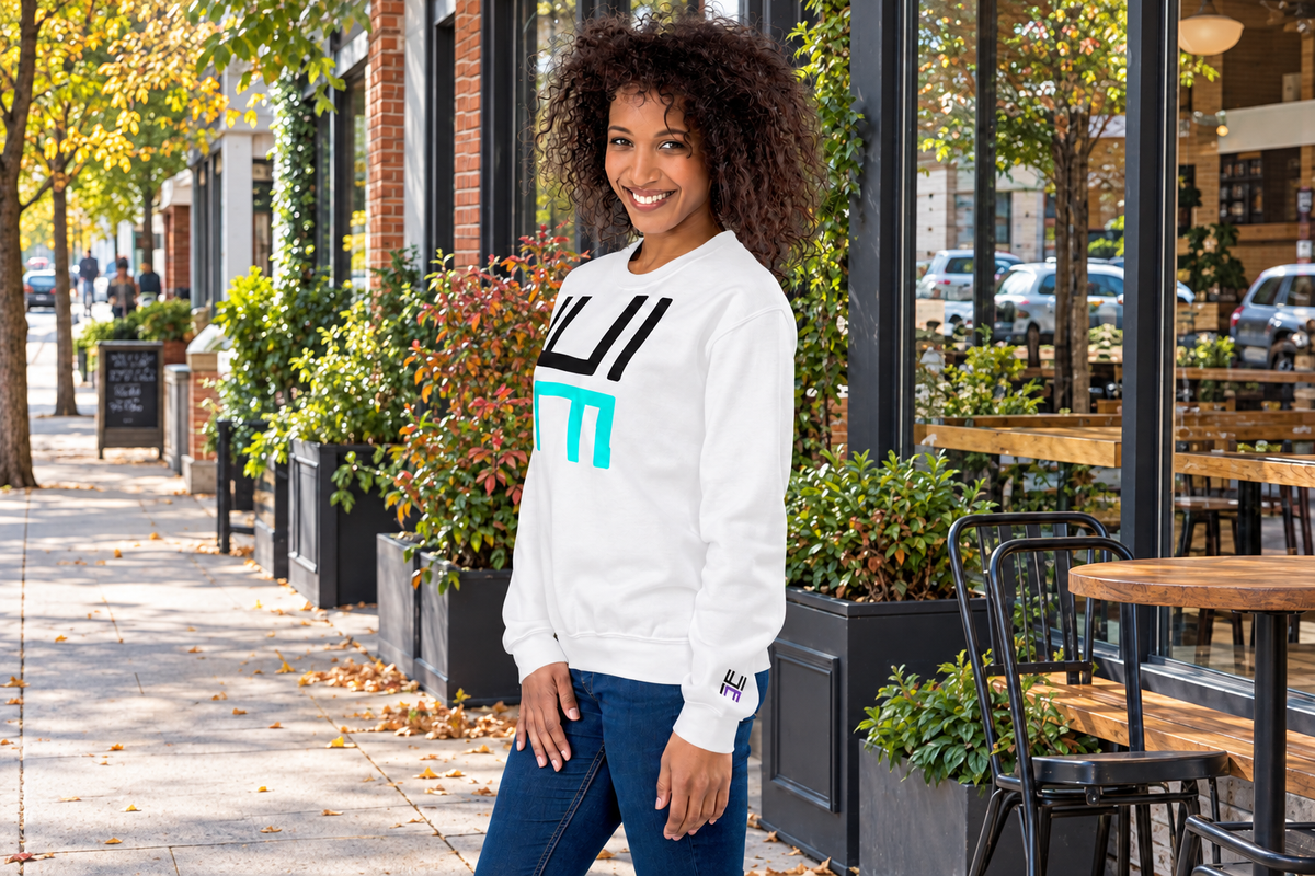 Model outside a café wearing a white Hustle Motivate Statement Crewneck with a black-and-teal front graphic and black-and-purple embroidered left sleeve