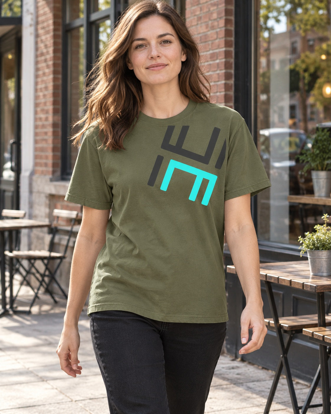 Lifestyle mockup of an adult wearing the Sage Hustle Motivate Perspective Tee with black jeans on a café sidewalk.