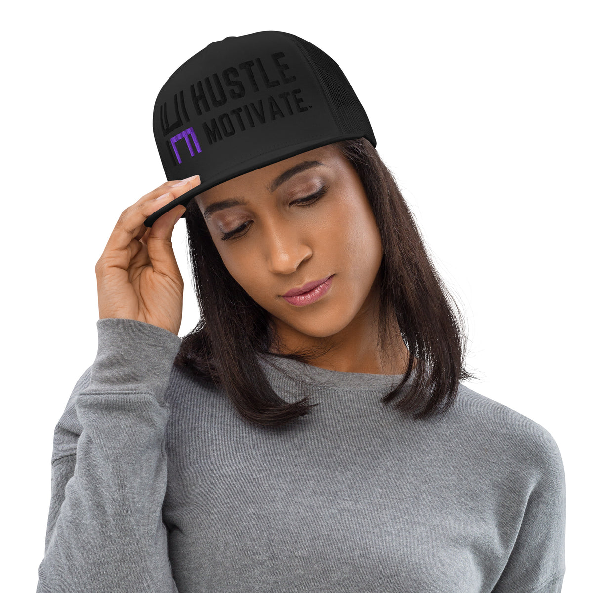 Model wearing the black Hustle Motivate Elevate trucker cap with tonal black lettering, a purple HM accent and black mesh panels