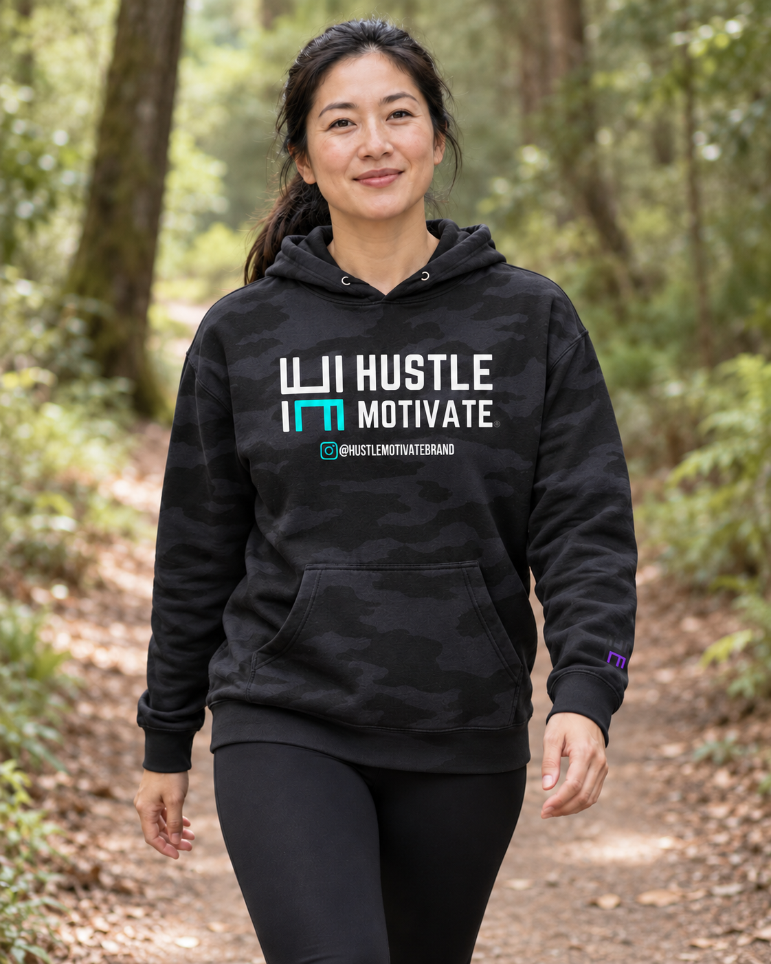 AI lifestyle mockup of the Black Camo Hustle Motivate hoodie worn on a woodland trail.