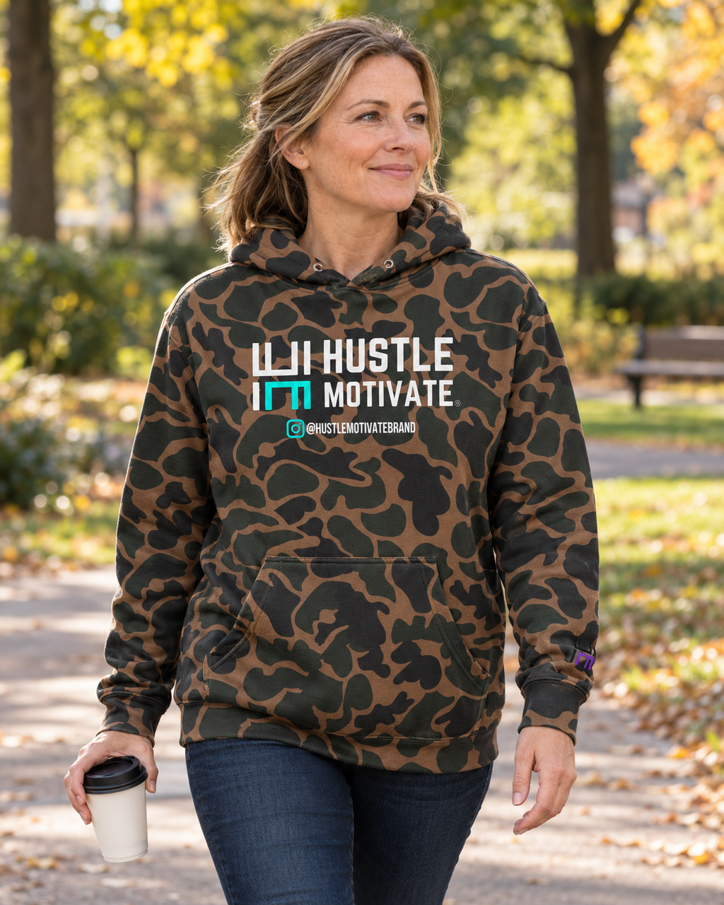 AI lifestyle mockup of the Duck Camo Hustle Motivate hoodie worn in an autumn park.