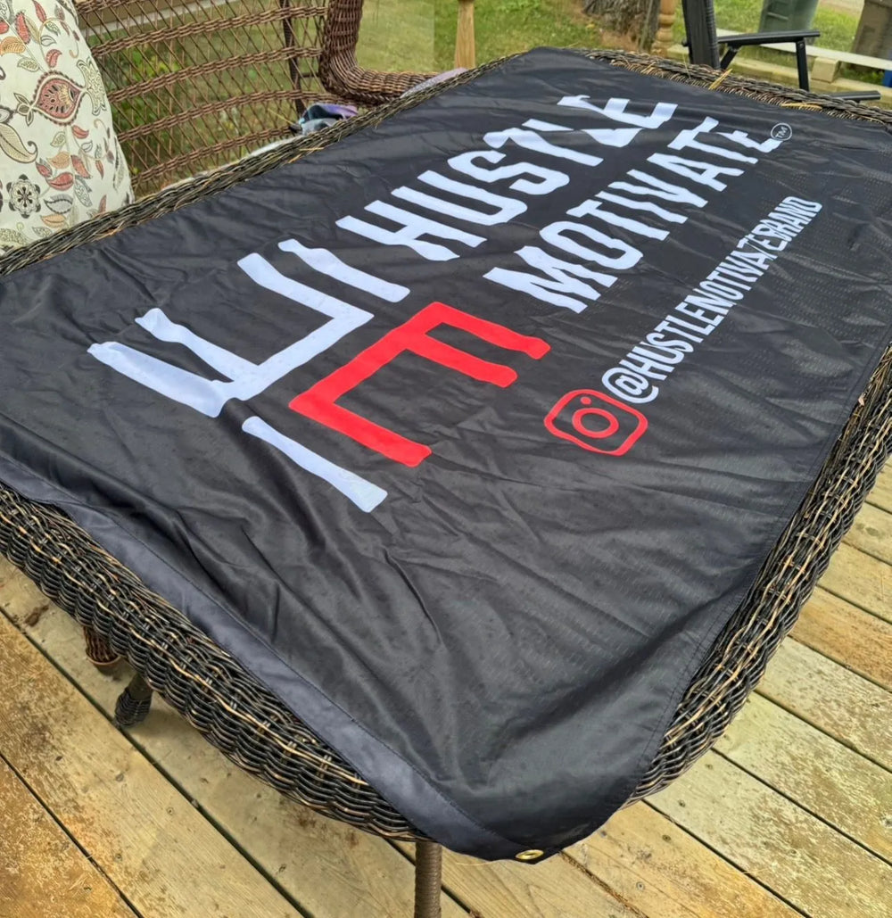 Black Hustle Motivate flag with white and red branding, photographed on outdoor seating.