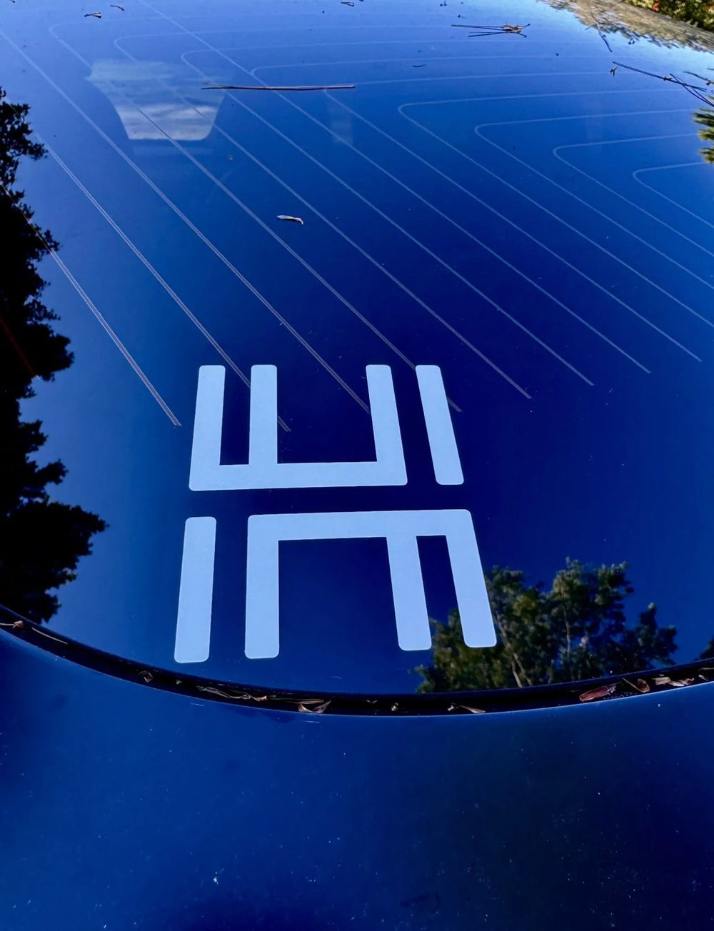 White HM monogram decal on a car window.