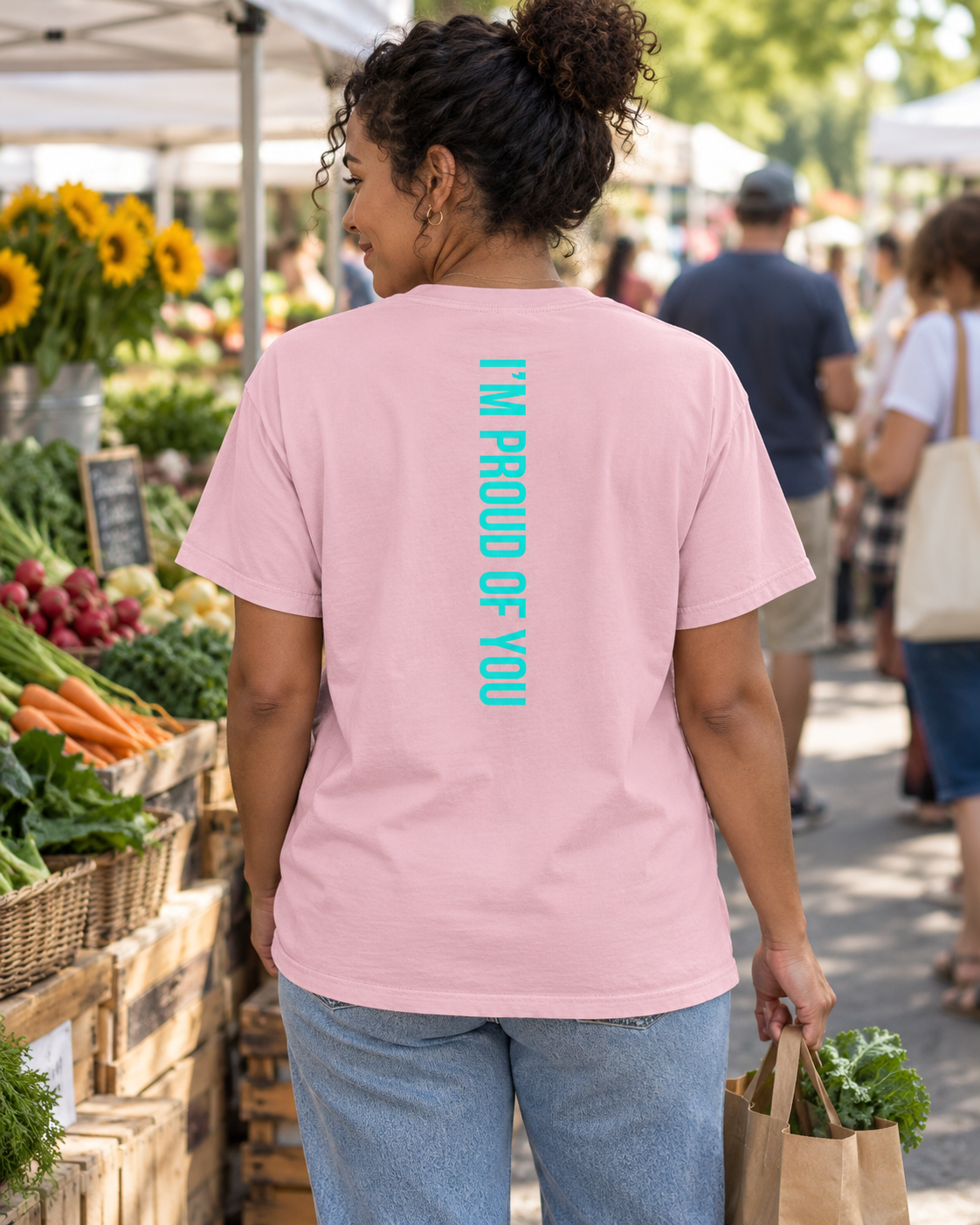 AI lifestyle mockup of the Blossom Hustle Motivate T-shirt worn at an outdoor market, showing the teal “I’M PROUD OF YOU” back design.
