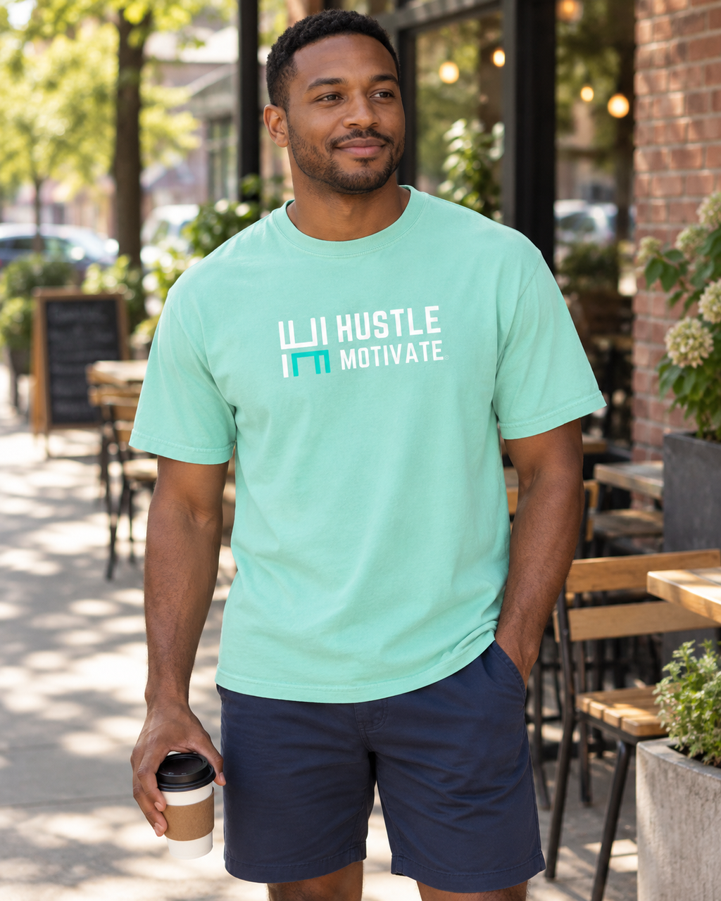 AI lifestyle mockup of the Chalky Mint Hustle Motivate T-shirt worn on a café patio, showing the white-and-teal front logo.