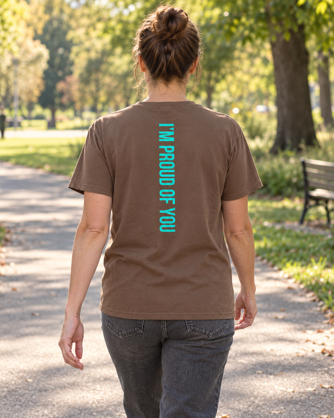 AI lifestyle mockup of the Espresso Hustle Motivate T-shirt worn in a park, showing the teal “I’M PROUD OF YOU” back design.