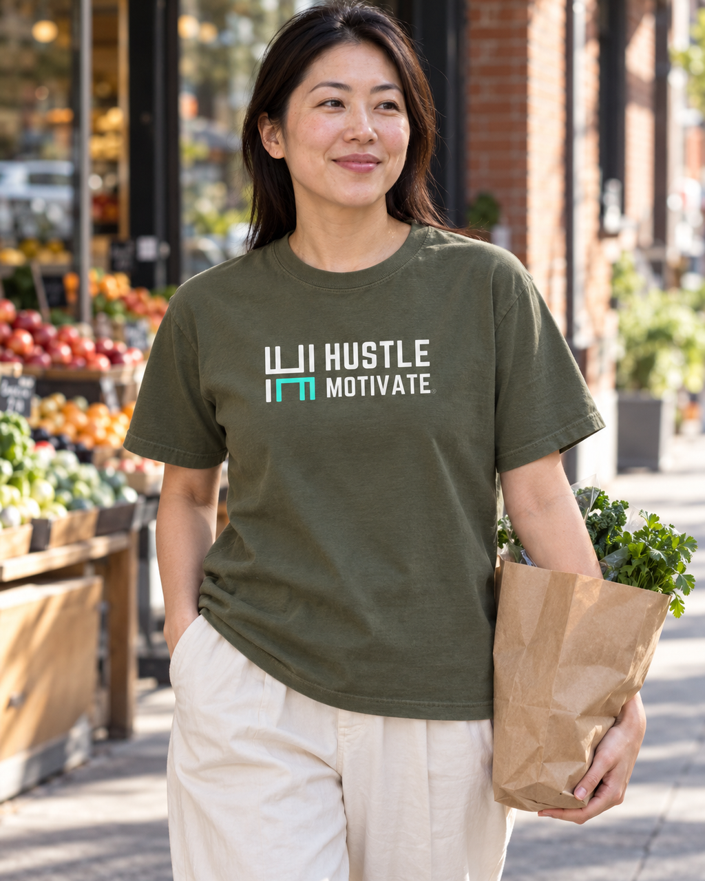 AI lifestyle mockup of the Sage Hustle Motivate T-shirt worn while carrying groceries, showing the white-and-teal front logo.